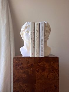 two books are sitting on top of a wooden block with a bust of a man