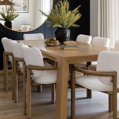 a wooden table with white chairs and a mirror on the wall behind it in a dining room