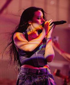 a woman holding a microphone in her right hand and wearing high waisted jeans on stage