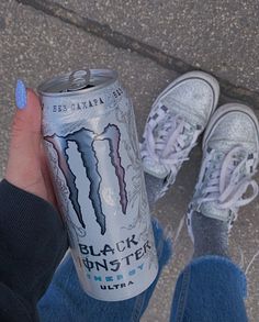 a person is holding up a can of black monster beer in front of their feet