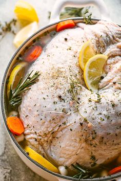 a chicken in a pot with lemons, carrots and rosemary garnish