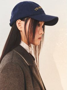 a woman with long hair wearing a blue hat and brown coat, looking off to the side