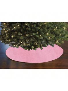 a christmas tree in a pink potted planter on a wooden floor with lights