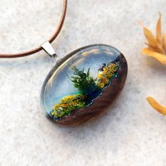 "🌿This pressed flower necklace is made by combining clear resin and a piece of hand carved walnut wood. 🌿A small mountain necklace was carved from walnut wood and a live moss,preserved moss was placed inside. 🌿This little moss art was made to look like a small piece of nature but also looks like a small terrarium necklace. 🌿This nature jewelry inspired by nature will be a great gift for nature lovers. 🌿The botanical necklace is absolutely unique as it is handmade and it is impossible to mak Nature-inspired Jewelry As A Gift With Natural Variations, Natural Wood Jewelry With Natural Variations As Gift, Natural Wood Jewelry With Variations As A Gift, Natural Wood Jewelry With Variations For Gift, Natural Wood Jewelry With Variations For Gifts, Nature-inspired Resin Pendant Necklace, Nature-inspired Resin Round Pendant Necklace, Nature-inspired Resin Round Pendant Necklaces, Nature-inspired Resin Necklaces With Round Pendant