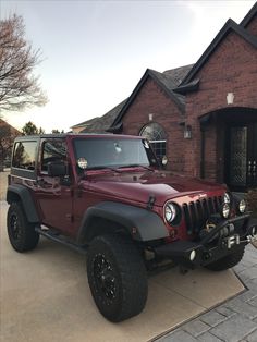 a red jeep is parked in front of a brick house with black tires and rims