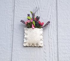 a white vase with flowers in it hanging on the side of a building or wall