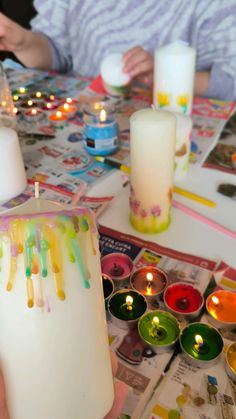 a person holding a lit candle in front of candles on a table with magazines and magazine pages