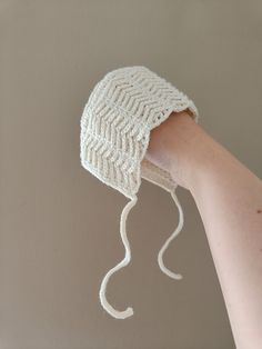 a white knitted hat being held by a person's hand with no hair