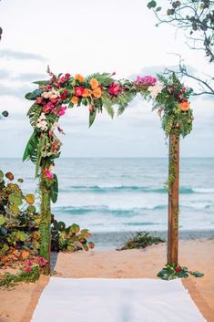 an outdoor wedding ceremony setup with flowers and greenery on the sand at the beach