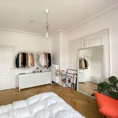 a bedroom with white walls and wooden floors, clothes on hangers in the closet