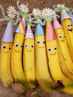 five bananas with faces painted on them and some daisies in the background, all lined up