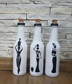 three white bottles with black silhouettes on them sitting on a wooden table next to a brick wall