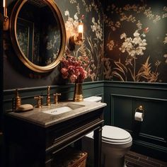 a bathroom with floral wallpaper and gold fixtures on the vanity, along with a white toilet