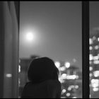 black and white photograph of woman looking out window at city lights