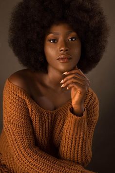 a woman with an afro is posing for a photo in front of a dark background