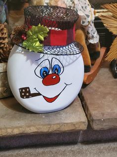 a white ceramic pot with a clown face painted on it's side, sitting on the ground