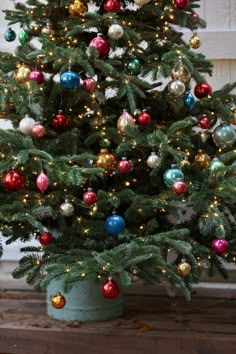 a small christmas tree with colorful ornaments in a blue pot on a wooden floor next to a window