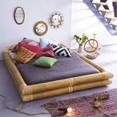 a bed made out of bamboo with lots of pillows on top of it and some plants in the background