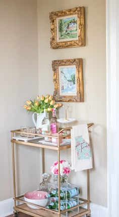 a gold bar cart with drinks and flowers on it in the corner of a room