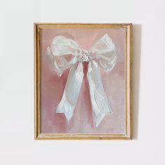 a painting of a white bow on a pink background in a gold frame with a light pink wall behind it