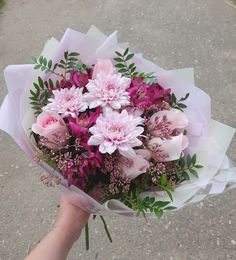 a person holding a bouquet of flowers in their hand on the ground with gravel behind them