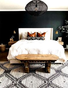 a bedroom with black walls, white bedding and wooden bench in the middle of the room