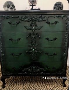 an ornate green chest of drawers with skulls on the top and bottom, in front of a white wall