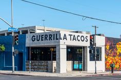 a street corner with a building painted blue and white in the background that says guerilla tacos