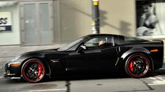 a black sports car with red rims parked on the street in front of a building