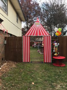 a red and white striped tent next to a wooden fence with balloons in the air