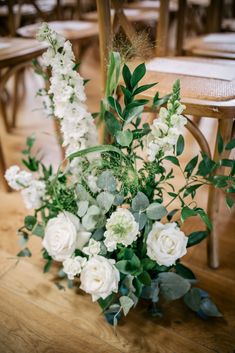 white flowers and greenery are arranged on the floor in front of two wooden chairs