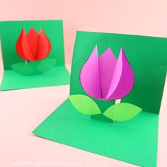 two folded paper flowers sitting on top of each other in front of green envelopes