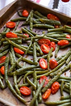 cooked green beans and tomatoes on a baking sheet ready to be baked in the oven