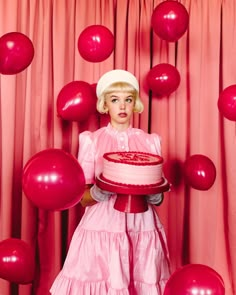 a woman holding a cake in front of balloons