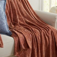 a couch with a blanket on top of it next to pillows and a vase in the background