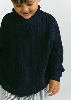 a young boy wearing a blue sweater and striped pants with his hands in his pockets