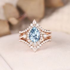 a ring with an aqua blue stone surrounded by white pearls and diamonds on a cushion