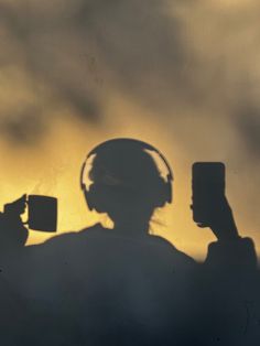 the shadow of a person holding a cell phone in front of their face with headphones on