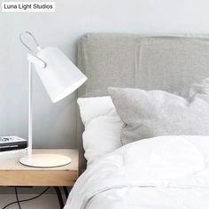 a bed with white sheets and pillows next to a lamp on a nightstand in a bedroom