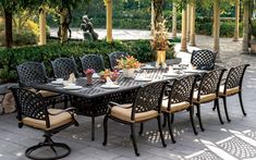 an outdoor dining table with eight chairs and plates on it, surrounded by greenery