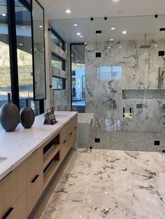 a bathroom with marble counter tops and large mirrors on the wall, along with two vases