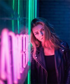 a beautiful young woman standing next to a neon sign