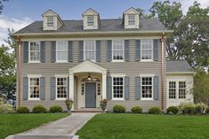 a large gray house with two story windows and blue shutters on the front door