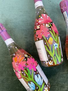 three wine bottles with flowers painted on them are sitting next to each other and one is empty