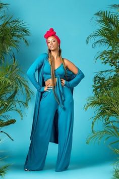 a woman standing in front of palm trees wearing a blue jumpsuit and red head scarf