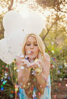 a woman blowing bubbles in front of her face with white balloons floating over her head