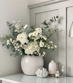 a vase filled with white flowers sitting on top of a table next to a mirror