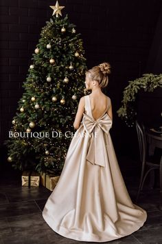 a woman standing in front of a christmas tree wearing a dress with a bow on the back