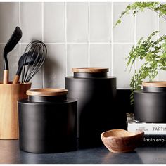 black kitchen utensils and wooden spoons are on the counter next to books