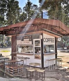 an outdoor coffee shop with tables and stools under a shade umbrella over the counter